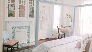 A bedroom with a bed, a chair, a vanity with a mirror, a fireplace, and a wardrobe with glass doors.