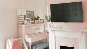 A living room with a fireplace, a television mounted above it, a bench, and a chair with a cushion.