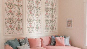 A cozy living room with a pink sofa, patterned wall art, a chandelier, and a traditional rug.