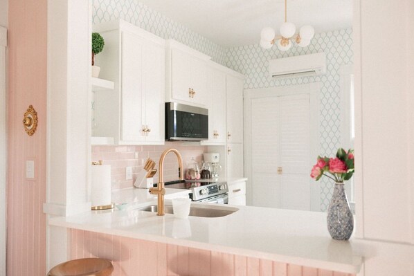 Una cocina moderna con armarios blancos, un microondas de acero inoxidable y una encimera blanca.