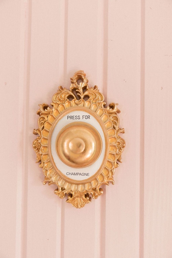 Un objet décoratif, doté d’un cadre doré, sur lequel on peut lire l’inscription « APPUYEZ ICI POUR DU CHAMPAGNE » sur un fond rose.