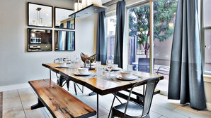 Zona pranzo con tavolo in legno apparecchiato per quattro persone, una panca e un lampadario moderno.