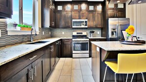 Una cucina moderna con mobili in legno scuro, elettrodomestici in acciaio inossidabile, un'ampia finestra e una sedia gialla.