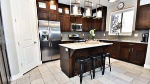 Una cocina moderna con armarios de madera oscura, electrodomésticos de acero inoxidable y una isla central con taburetes de bar.