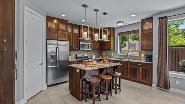 Una cocina moderna con una isla central, electrodomésticos de acero inoxidable, armarios de madera e iluminación colgante.