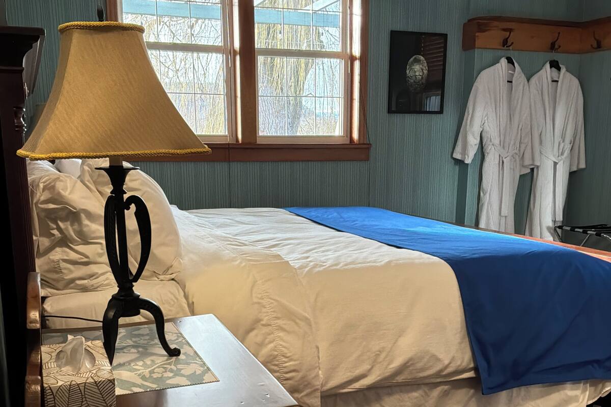 Une pièce comprenant un lit, une lampe, une fenêtre et un porte-manteau fixé au mur.