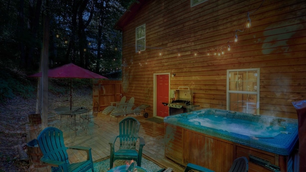 Una cabaña de madera con jacuzzi, mobiliario exterior y una fogata.