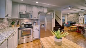 Una cocina moderna con electrodomésticos de acero inoxidable, una pared de acento de piedra y una mesa de comedor de madera con una planta.
