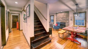 Amplia sala de estar con escalera de madera, pared de acento de piedra y una mesa de comedor para cuatro personas.