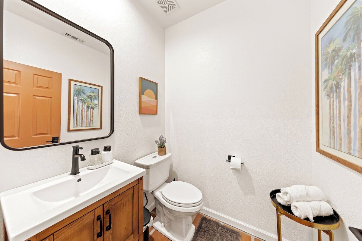 Une salle de bain avec un lavabo blanc, un meuble en bois, des toilettes et une petite table avec des serviettes.