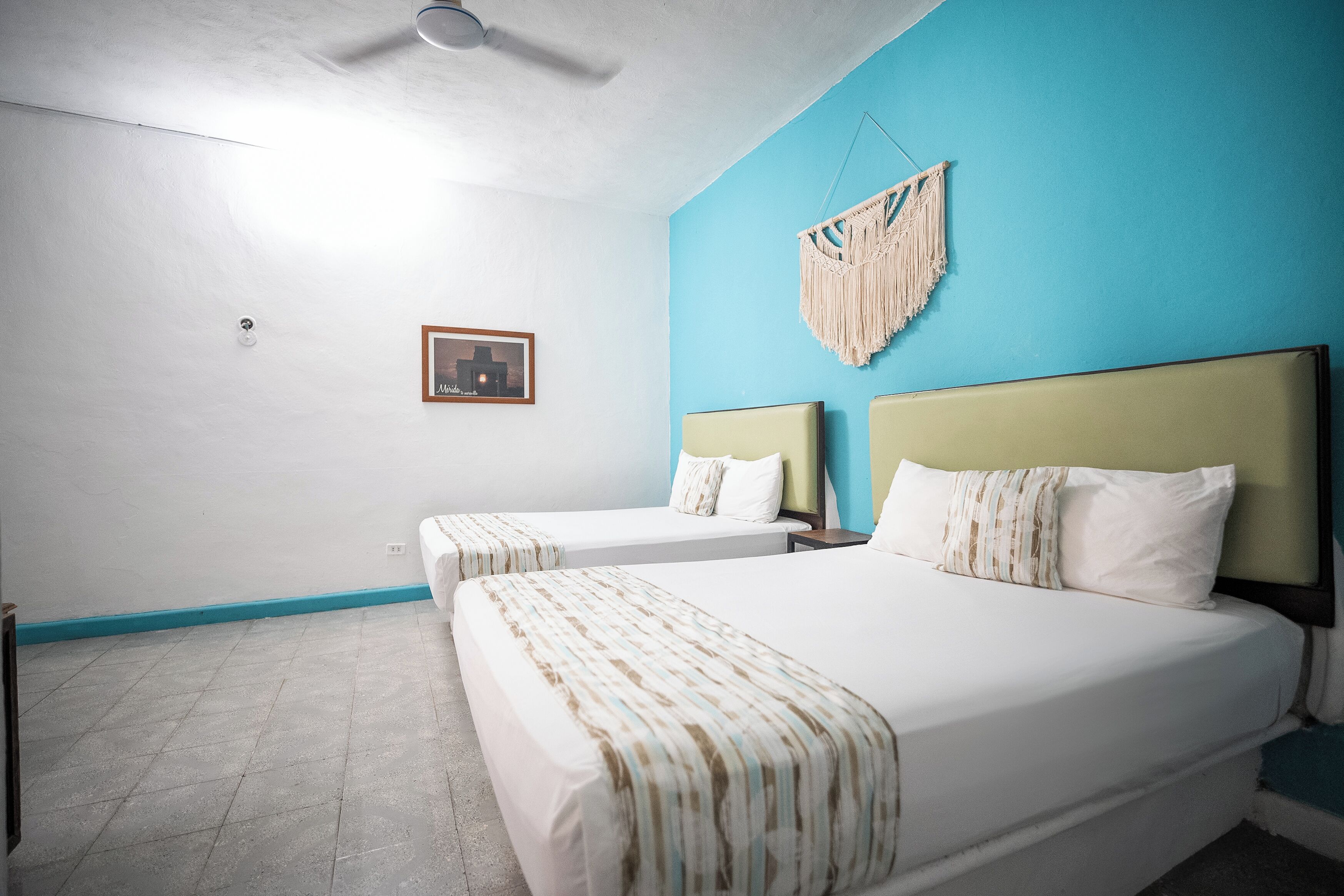 Habitación de hotel con dos camas, ventilador de techo, un cuadro en la pared y una pared de acento azul.
