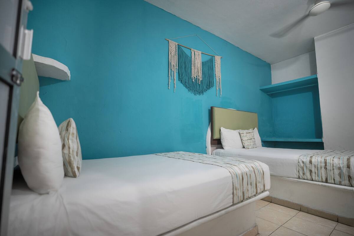 A room with two beds, a ceiling fan, and a wall-mounted macrame decoration.