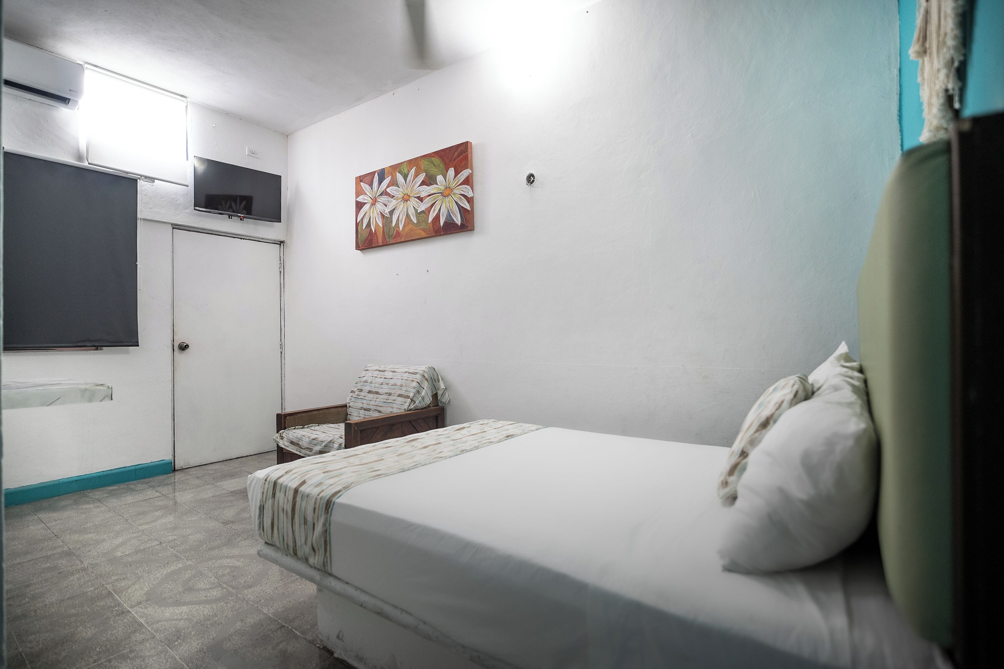 A bedroom with a bed, a chair, a TV mounted on the wall, and a door.