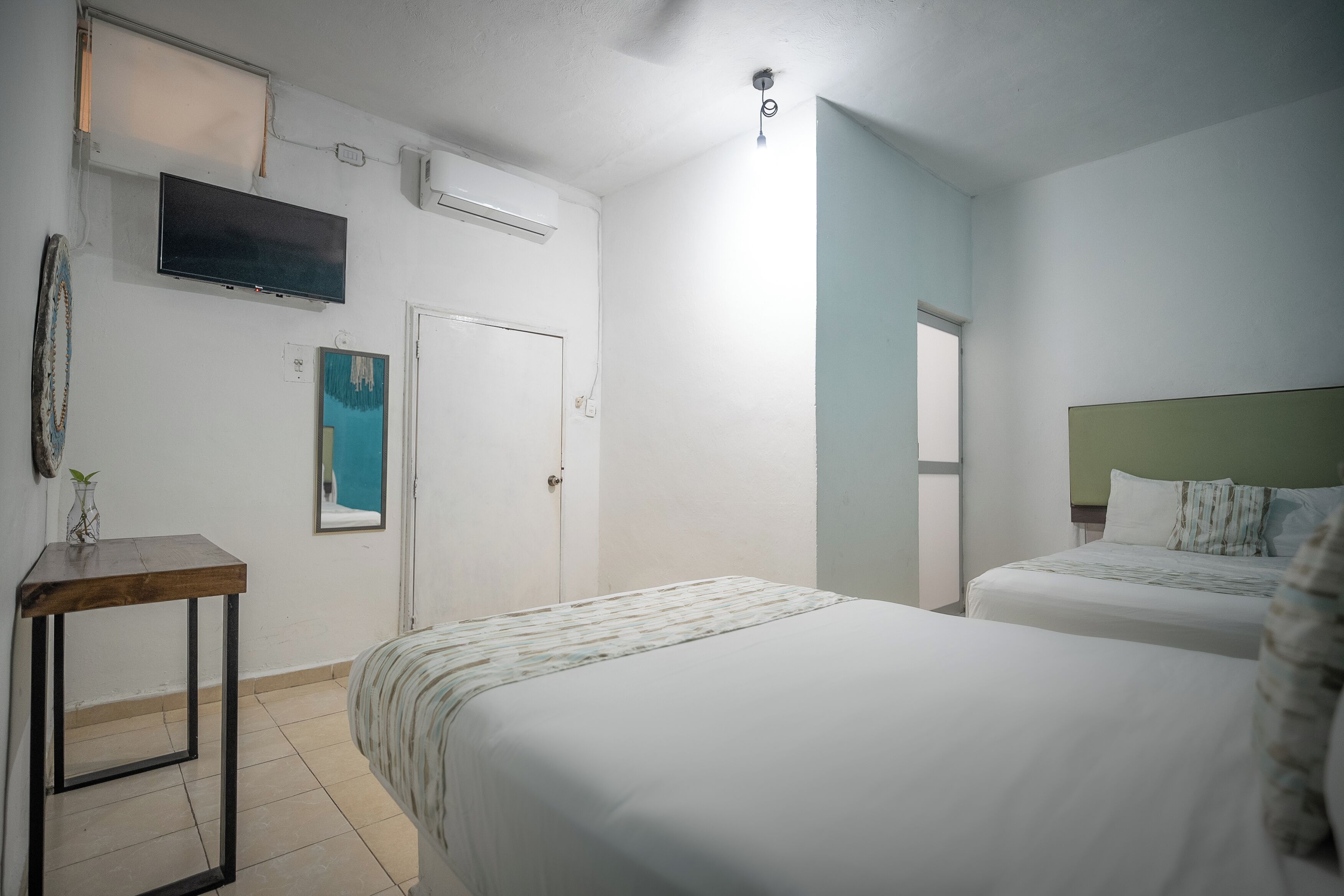 A hotel room with two beds, a TV mounted on the wall, a small table, and a door.