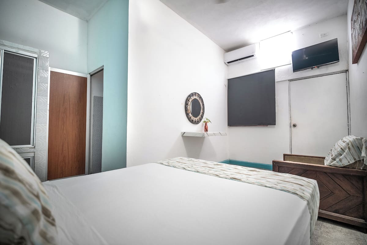 A bedroom with a bed, a wooden headboard, a wall-mounted TV, a wardrobe, and a mirror.