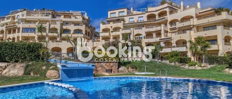 Piscina con borde de piedra y fuente de agua, rodeada de césped cuidado y grandes rocas.