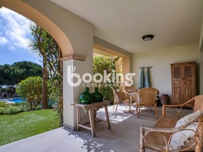 A covered outdoor patio with wicker furniture, a table, and a view of a swimming pool and greenery. - GROUND FLOOR WITH TERRACE FOR 4 PEOPLE WITH SEA VIEWS AND AT THE FOOT OF THE POO (Sant Feliu de Guíxols)