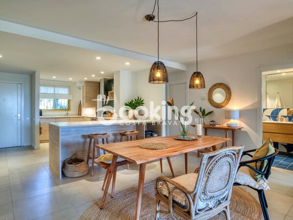 A modern kitchen with a central island, pendant lighting, and a dining area with wicker chairs.