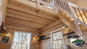 Een houten cabin interieur met een trap, grote ramen en een bord met de tekst 'The Oasis Hocking Hills Luxury Lodging'.
