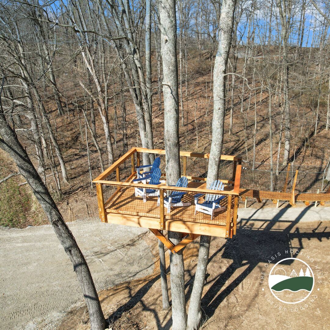 Une terrasse en bois avec des chaises bleues et une table, entourée d’arbres.
