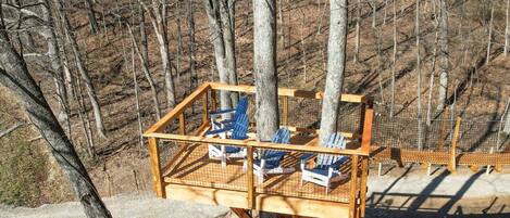 Une terrasse en bois avec des chaises bleues et une table, entourée d’arbres.