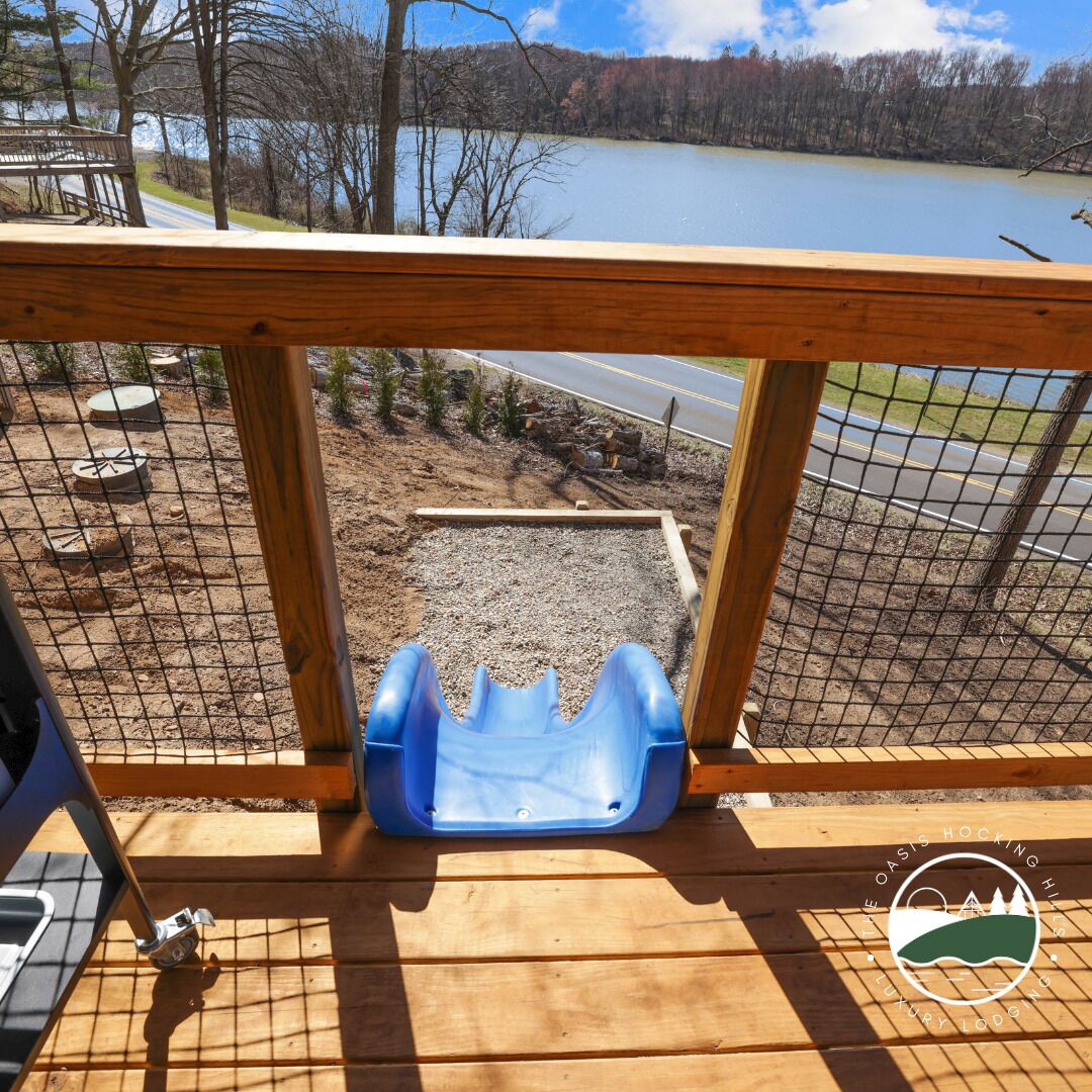 Eine Holzterrasse mit einer blauen Kunststoffrutsche, einem Metallstuhl und einer hölzernen Bank.