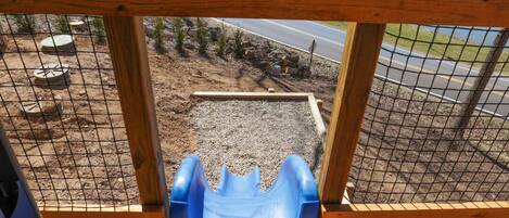 Eine Holzterrasse mit einer blauen Kunststoffrutsche, einem Metallstuhl und einer hölzernen Bank.