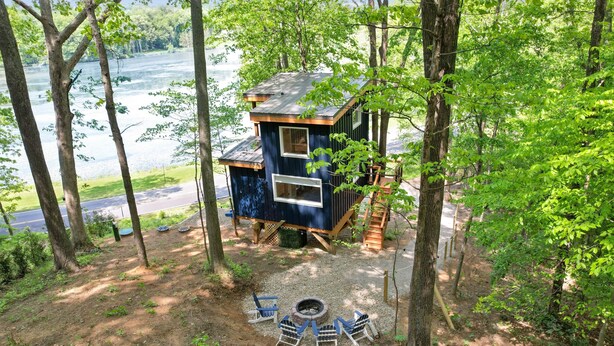 Een boomhut met een klein terras, een vuurkuil en uitzicht op een meer.