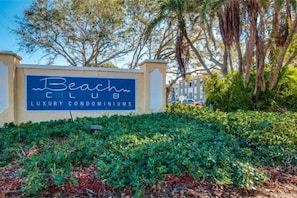 A sign for 'Beach Club Luxury Condominiums' with a landscaped garden in the foreground.