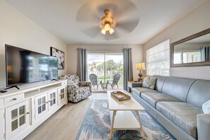A living room with a flat-screen TV, a sofa, a coffee table, and a ceiling fan.