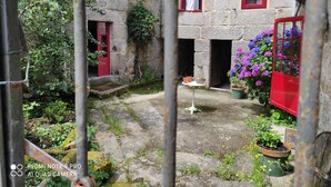 A stone building with red-framed windows, a red door, and a small garden area with potted plants and flowers.