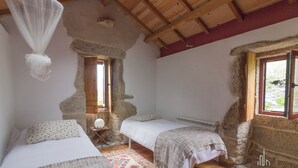 A rustic bedroom with two beds, a stone wall, and a wooden ceiling.