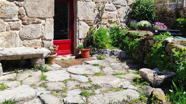 A stone building with a red door, potted plants, and a stone pathway.