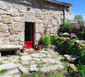 Un bâtiment en pierre avec une porte rouge, des plantes en pot et un chemin en pierre.
