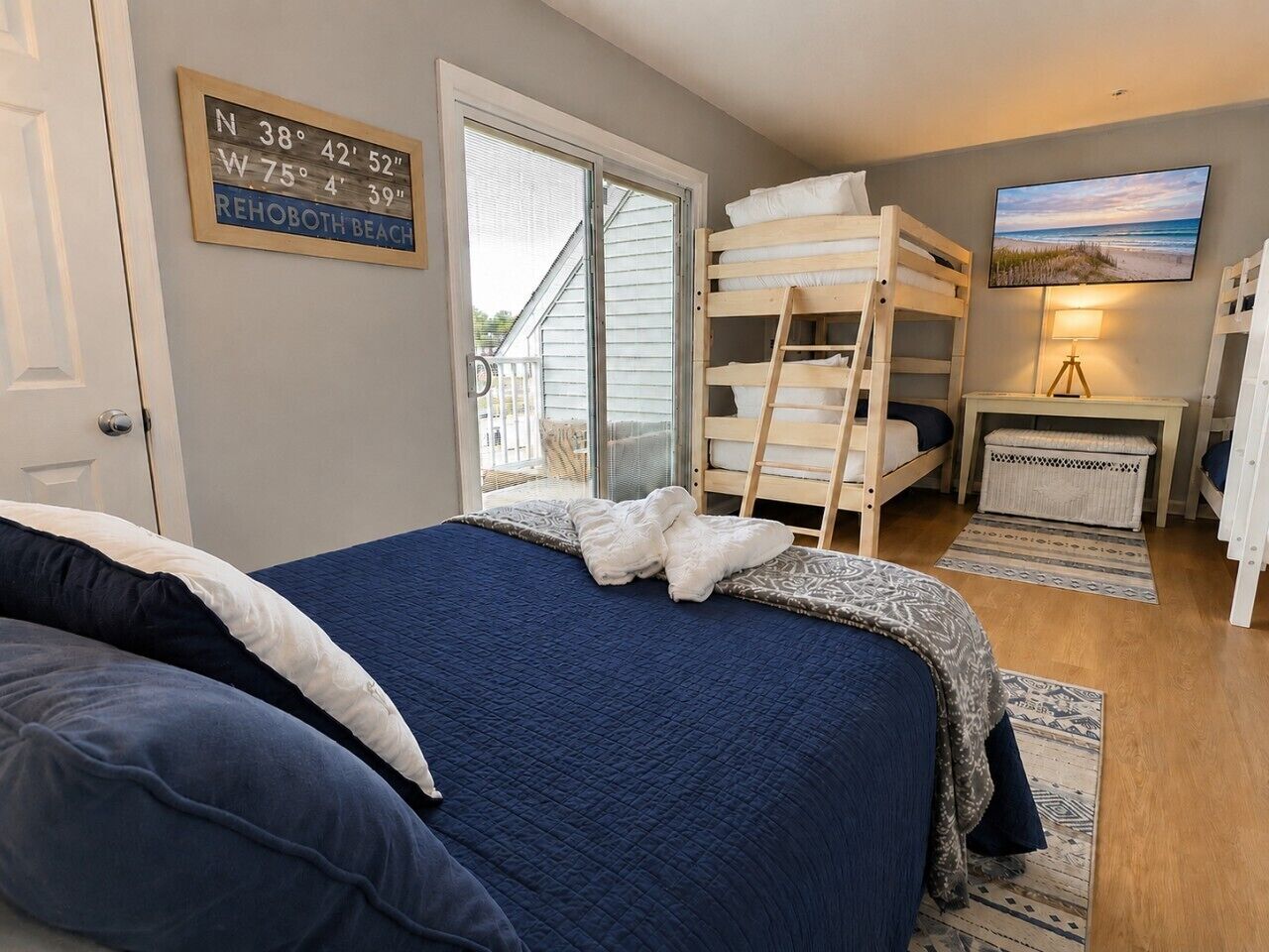 Een slaapkamer met een bed, stapelbedden, een televisie en een raam met uitzicht op het strand.