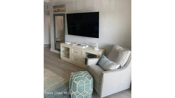 A living room with a flat-screen TV mounted on the wall, a light-colored sofa, a matching ottoman, and a white console table with decorative items.