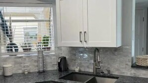 A modern kitchen with white cabinets, a granite countertop, a built-in sink, and a window with blinds.