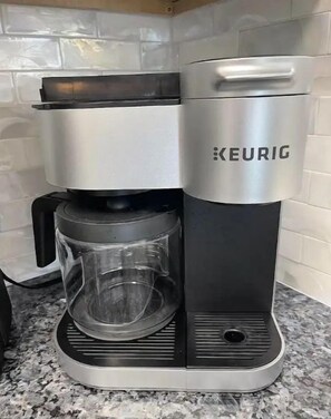 Une machine à café Keurig dotée d’une verseuse en verre et d’un bac de récupération, posée sur un comptoir en granit.