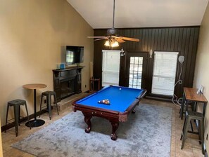 A pool table in a room with a ceiling fan, a television, and a fireplace.