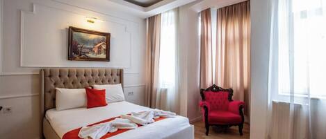 A hotel room with a large bed, a red armchair, a painting on the wall, and a window with curtains.