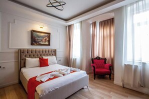 A hotel room with a large bed, a red armchair, a painting on the wall, and a window with curtains.