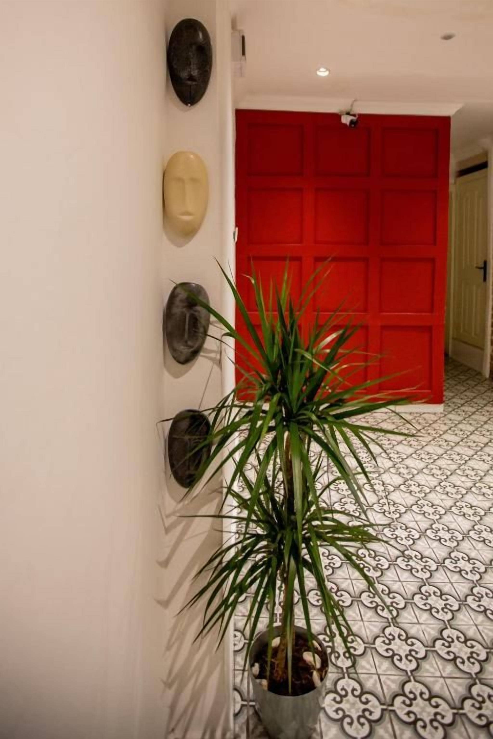 A hallway with a red door, a potted plant, and wall-mounted masks.