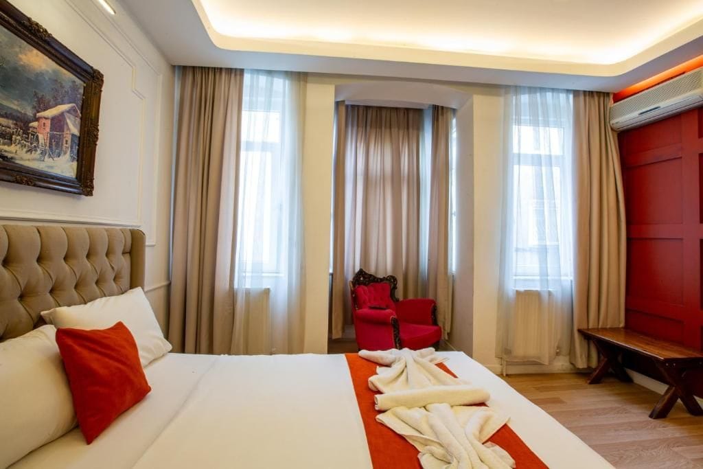 A hotel room with a large bed, a red chair, and a painting on the wall.