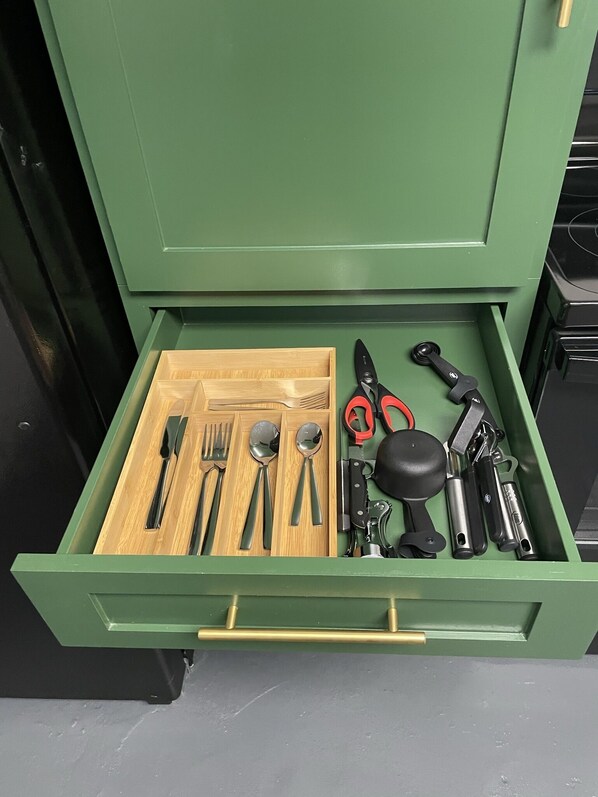 A drawer with a wooden tray containing cutlery, a spoon, a fork, a knife, and a pair of scissors.