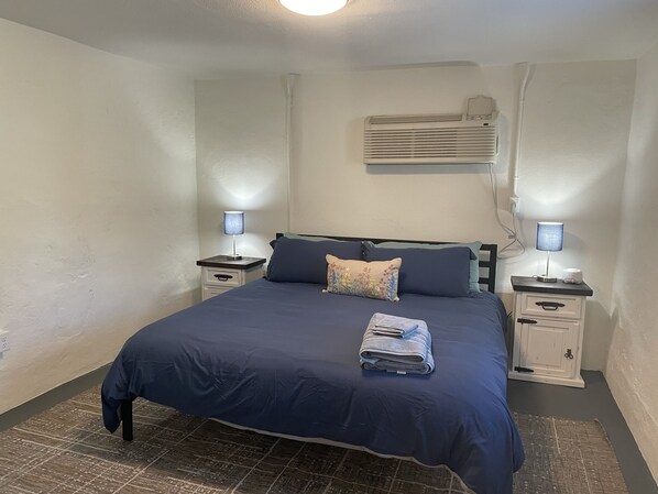 A bedroom with a bed, two bedside tables, an air conditioning unit, and a patterned rug. - NEW! Petite Palace on Park Ave (Hot Springs)