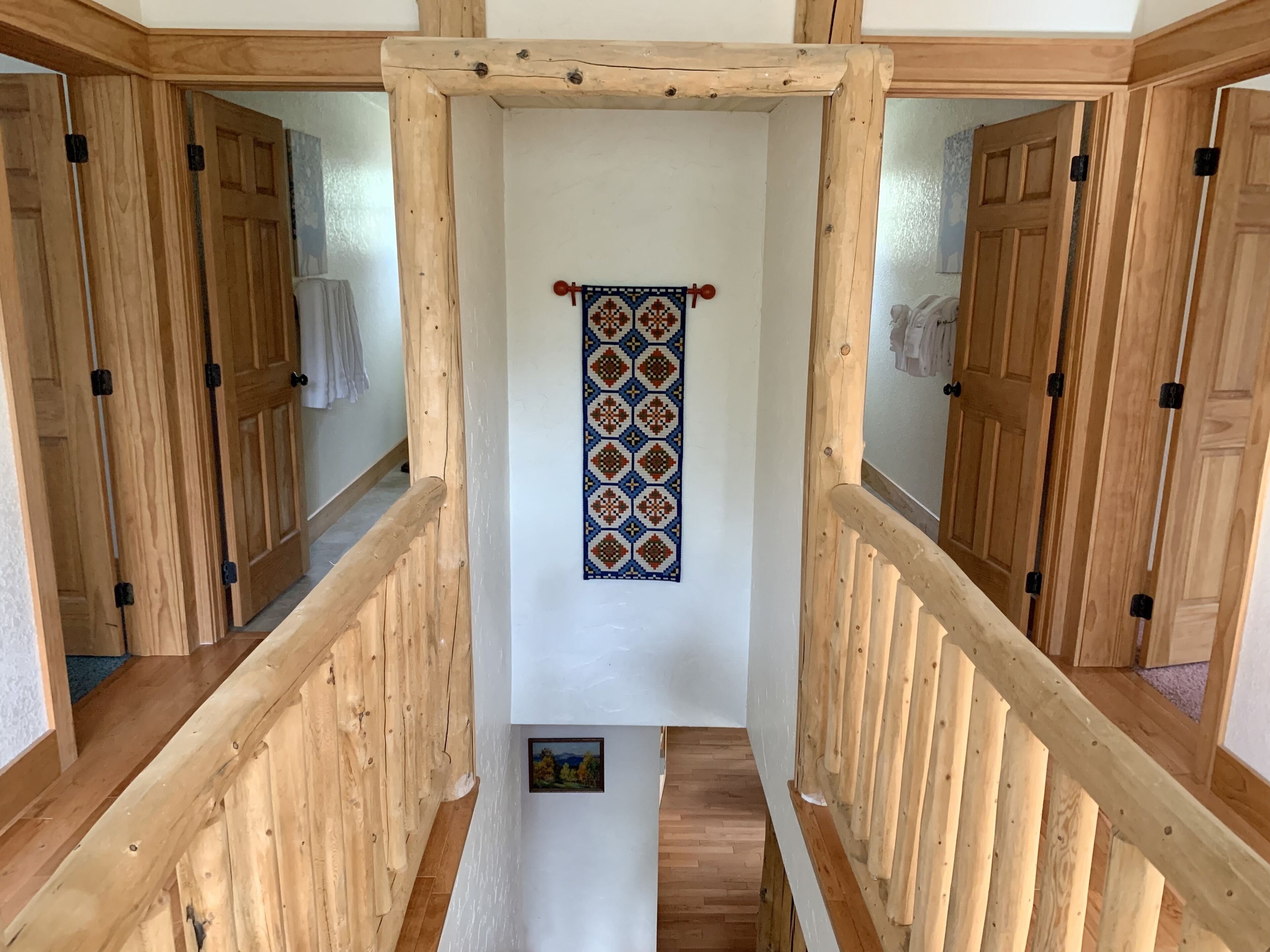 A wooden staircase with a handrail leading to a room with a patterned wall hanging.