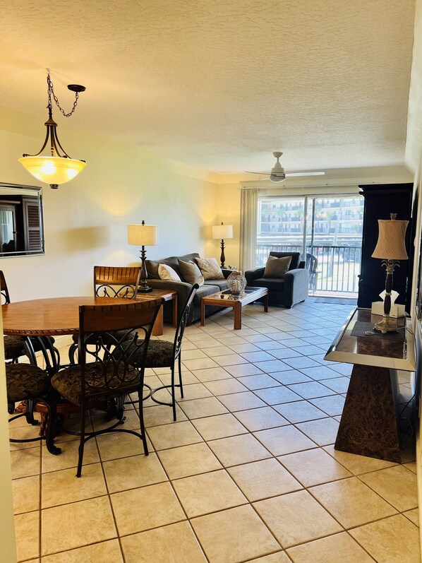 A spacious living area with a dining table, chairs, sofas, and a balcony with a view.