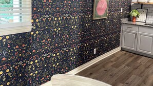 A kitchen with a dark floral wallpaper, a window with blinds, a framed picture on the wall, and a wooden chair. - Sweet Magnolias Home: Walk to Square (Covington)