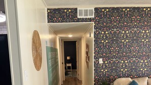 A hallway with a wooden floor, a patterned wall, a couch with pillows, and a small table with a lamp. - Sweet Magnolias Home: Walk to Square (Covington)