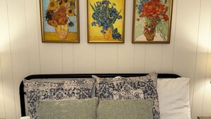 A bed with patterned pillows, a headboard, and three framed paintings of flowers on the wall. - Sweet Magnolias Home: Walk to Square (Covington)